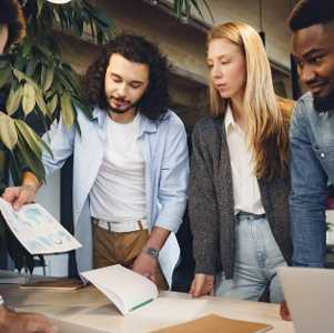 four people standing around a desk looking at reports